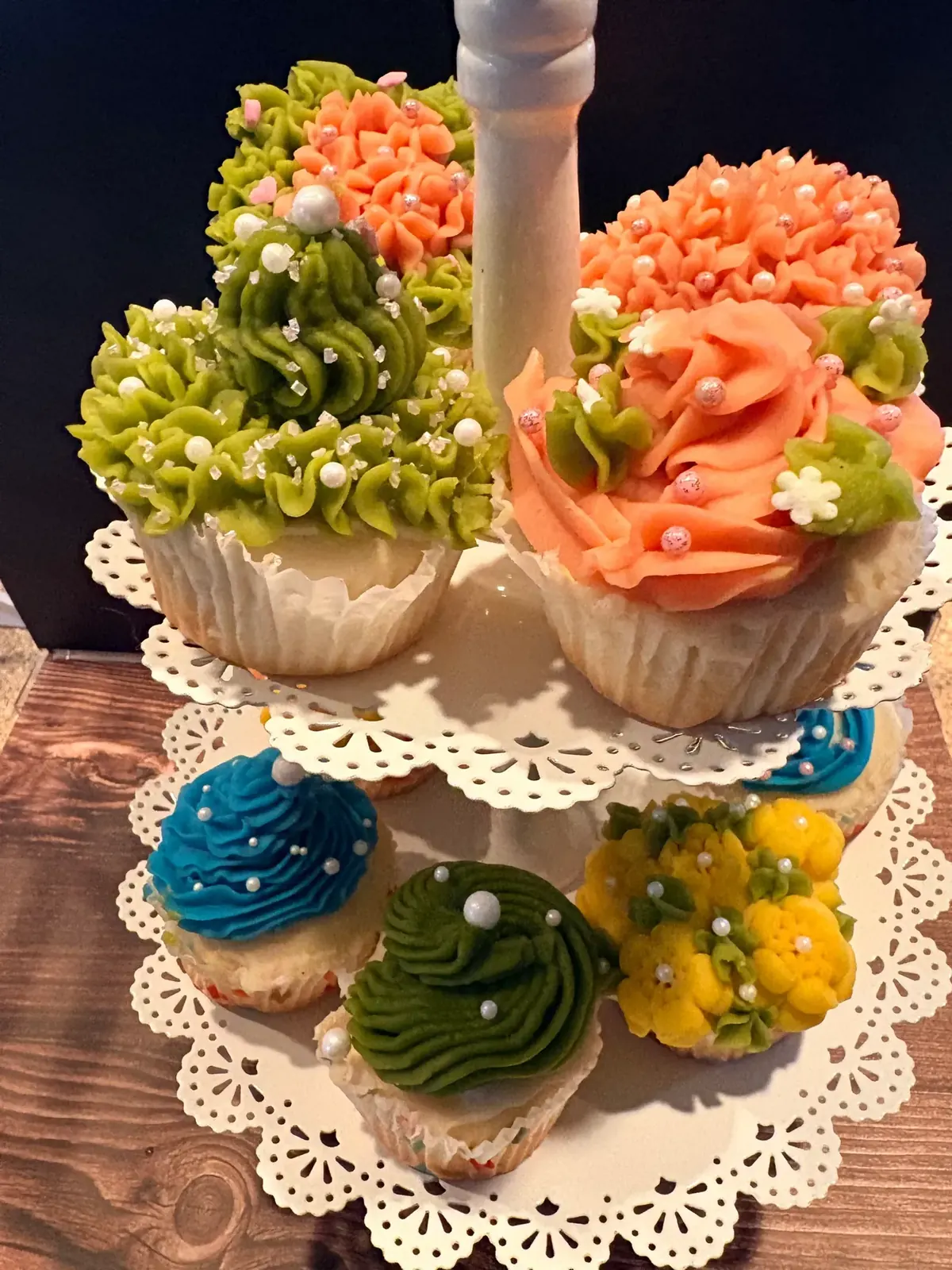 Tiered stand of cupcakes piped with buttercream flowers in green, coral, blue and yellow